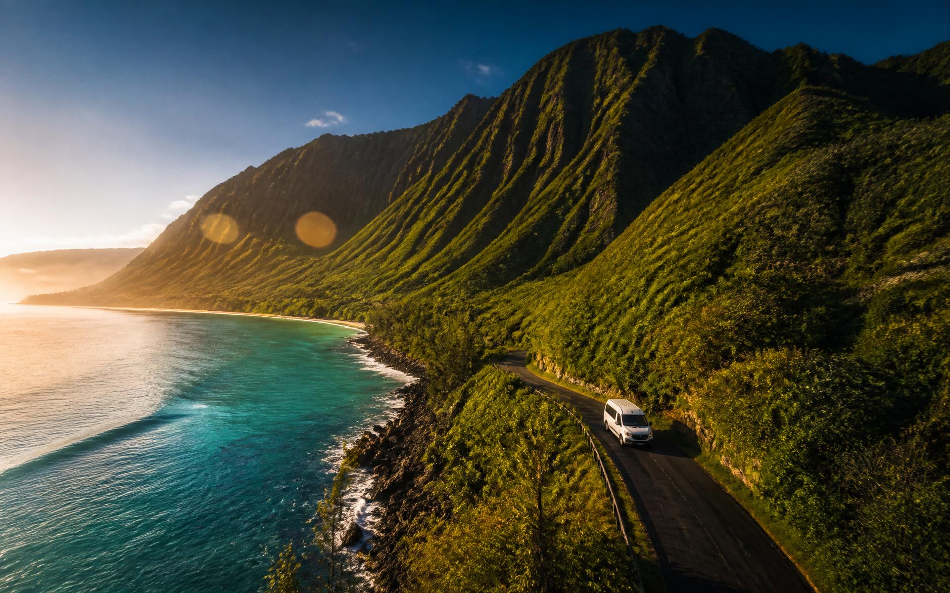 Aerial view of Oʻahu's turquoise coast at golden hour with a white passenger van on a winding coastal road